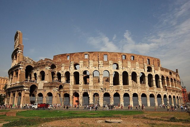 Vista panorâmica externa do Coliseu de Roma mostrando os quatro níveis de arcos, estrutura parcialmente arruinada e turistas visitando o monumento histórico