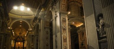 Interior da Basílica de São Pedro no Vaticano mostrando nave central com colunas monumentais, teto decorado dourado, baldaquino de Bernini e turistas visitando.