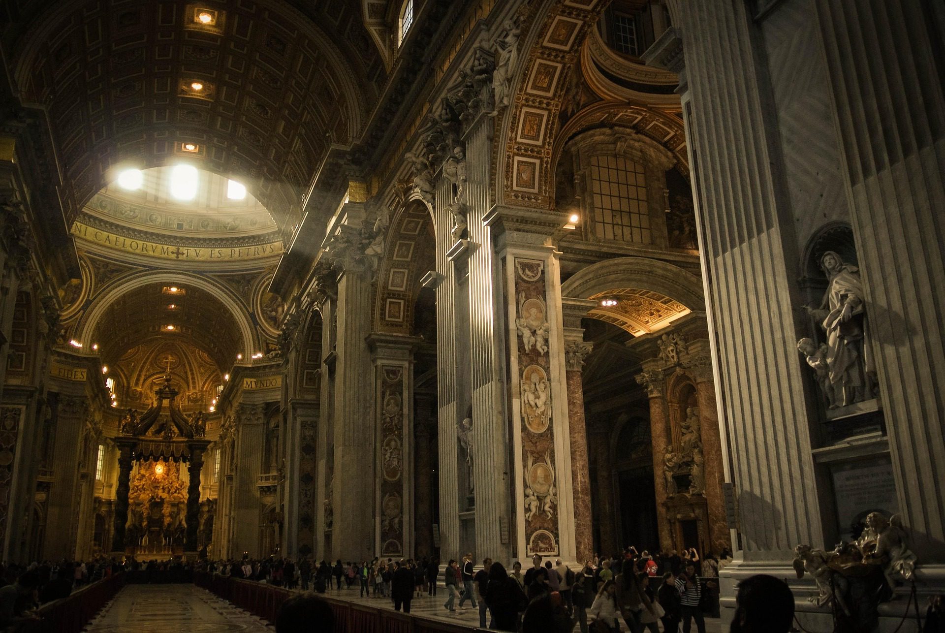 Interior da Basílica de São Pedro no Vaticano mostrando nave central com colunas monumentais, teto decorado dourado, baldaquino de Bernini e turistas visitando.