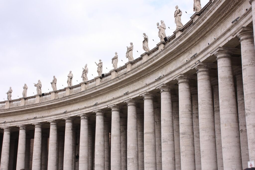 Colunatas da Praça de São Pedro no Vaticano com colunas de travertino e estátuas de santos no topo.
