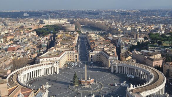 Vista panorâmica da Praça de São Pedro com colunatas de Bernini, obelisco central, Via della Conciliazione e Castel Sant'Angelo ao fundo.