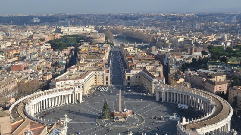 Vista panorâmica da Praça de São Pedro com colunatas de Bernini, obelisco central, Via della Conciliazione e Castel Sant'Angelo ao fundo.