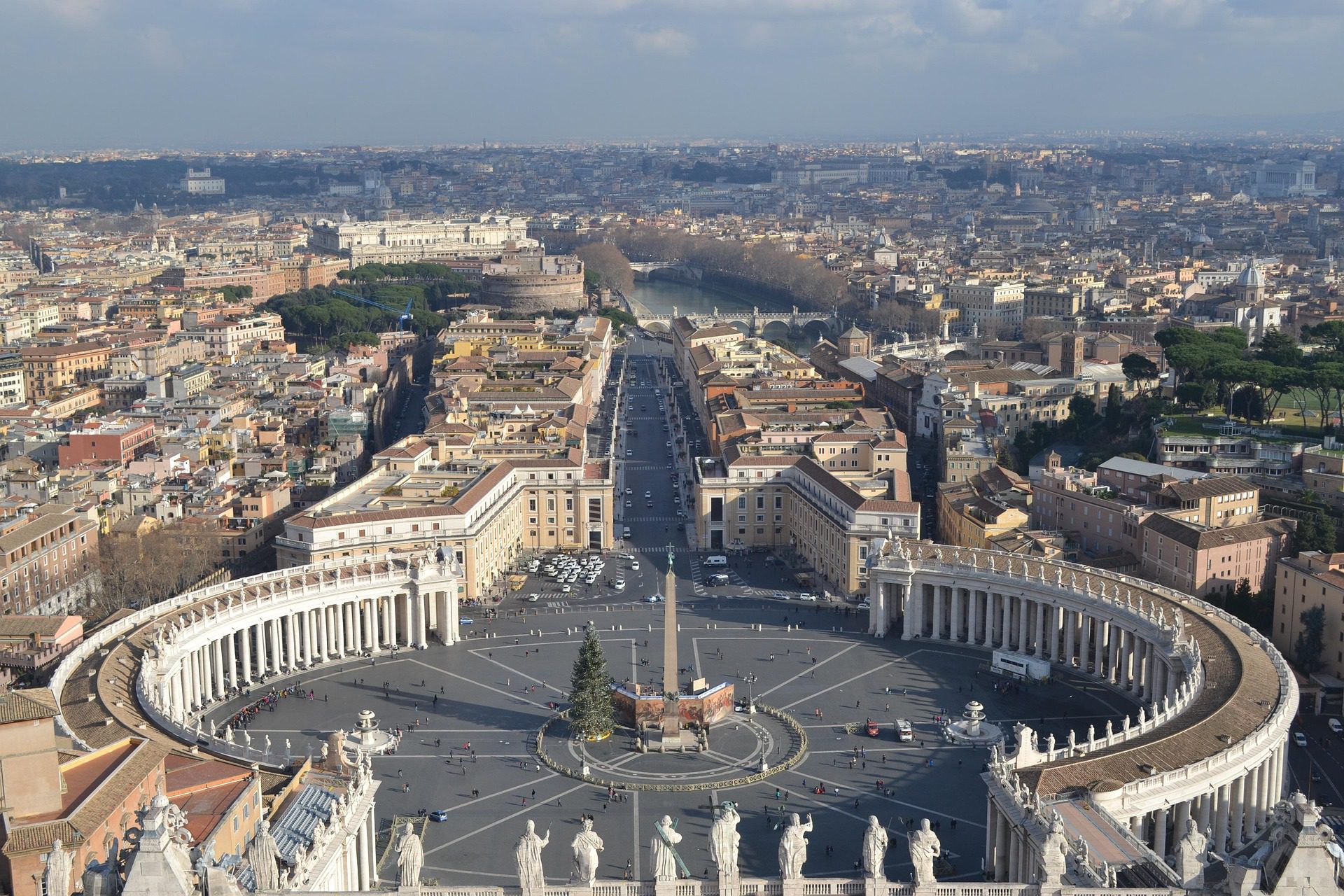 Vista panorâmica da Praça de São Pedro com colunatas de Bernini, obelisco central, Via della Conciliazione e Castel Sant'Angelo ao fundo.
