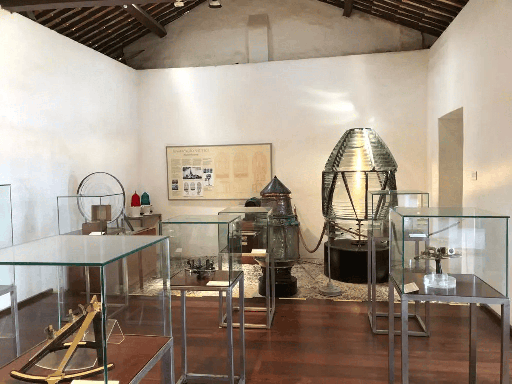 Interior do Museu Náutico da Bahia no Forte de Santo Antônio da Barra em Salvador, mostrando vitrines com instrumentos de navegação, lente de Fresnel de farol, sextantes e equipamentos náuticos históricos