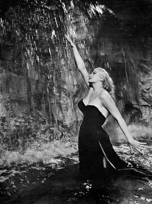 Fotografia clássica em preto e branco de mulher com vestido preto elegante sob cascata de água, cena icônica do cinema dos anos 1950-1960