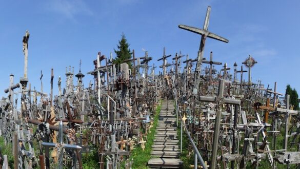 Colina das Cruzes em Šiauliai, Lituânia, com milhares de cruzes de madeira e metal, caminho de madeira e céu azul claro.