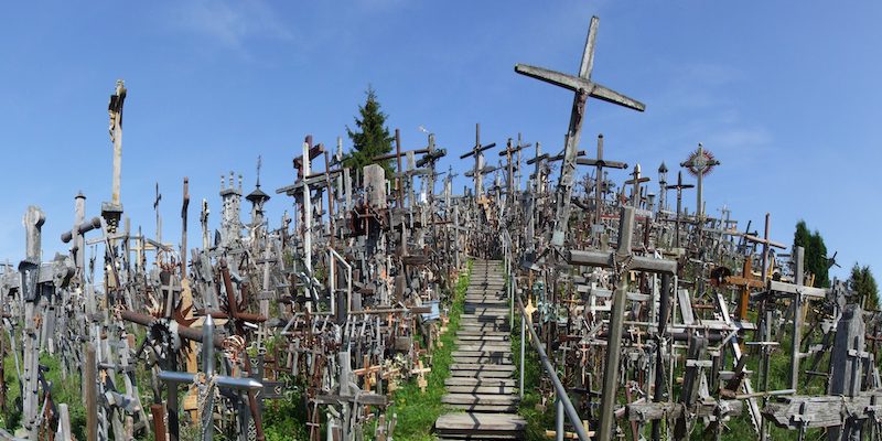 Colina das Cruzes em Šiauliai, Lituânia, com milhares de cruzes de madeira e metal, caminho de madeira e céu azul claro.