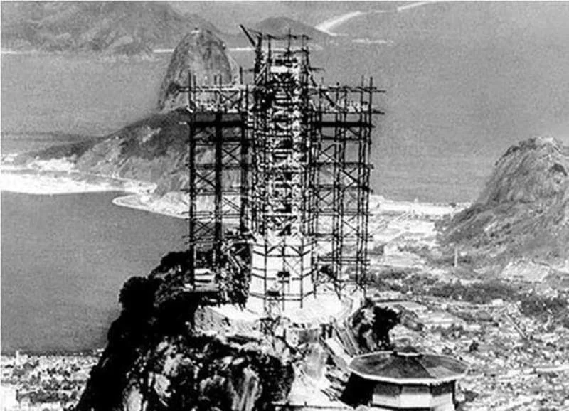 Fotografia histórica em preto e branco da construção do Cristo Redentor no Corcovado, Rio de Janeiro, mostrando andaimes e estrutura em construção com o Pão de Açúcar ao fundo, década de 1920-1930