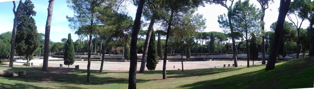 Jardins da Villa Borghese em Roma com árvores altas, gramado verde e área aberta de areia sob céu azul
