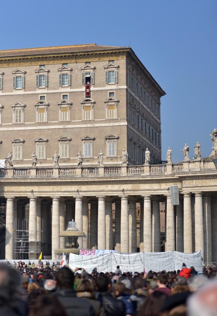 Palácio Apostólico no Vaticano com janelas dos apartamentos papais e colunatas de Bernini na Praça de São Pedro, com multidão de turistas e fiéis