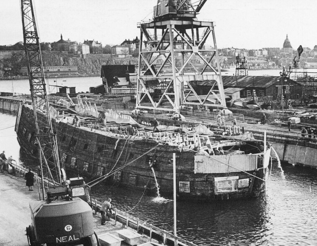 Foto histórica em preto e branco do resgate do navio Vasa em 1961, mostrando o casco sendo içado por guindastes no porto de Estocolmo, Suécia
