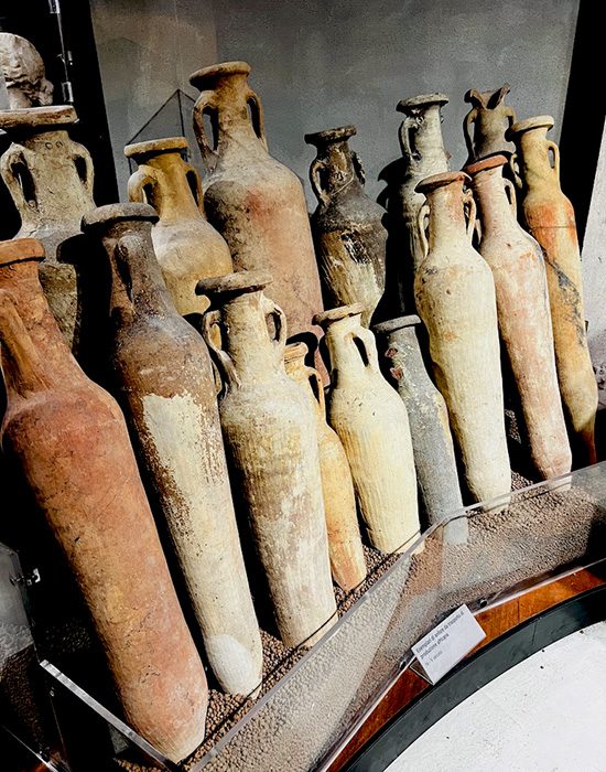 Coleção de ânforas romanas antigas e cerâmicas arqueológicas expostas em museu, mostrando vasos de armazenamento de diferentes tamanhos e cores do período imperial romano