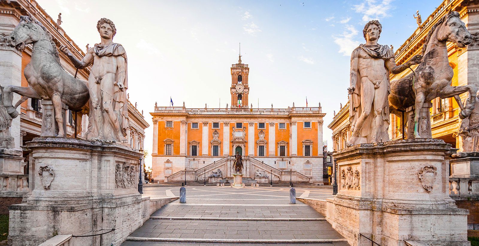 Piazza del Campidoglio em Roma mostrando estátuas dos Dioscuri (Castor e Pólux) com cavalos, Palazzo Senatorio com fachada laranja e torre do relógio, escadaria monumental e praça simétrica projetada por Michelangelo