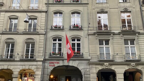 Einstein Haus em Berna Suíça, edifício histórico com arquitetura clássica europeia, bandeira suíça vermelha, arcadas e entrada do museu onde Albert Einstein viveu e desenvolveu a Teoria da Relatividade