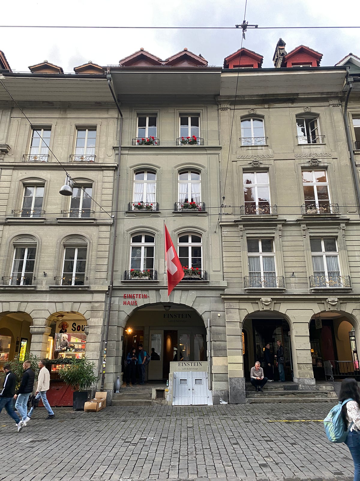 Einstein Haus em Berna Suíça, edifício histórico com arquitetura clássica europeia, bandeira suíça vermelha, arcadas e entrada do museu onde Albert Einstein viveu e desenvolveu a Teoria da Relatividade