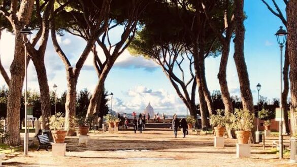 Avenida arborizada com pinheiros italianos em Roma mostrando caminho com vasos de terracota, postes de luz e vista panorâmica para a cúpula da Basílica de São Pedro no Vaticano ao fundo