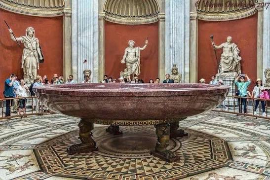 Grande bacia de pórfiro no centro da Sala Rotonda dos Museus do Vaticano, cercada por estátuas clássicas e visitantes.