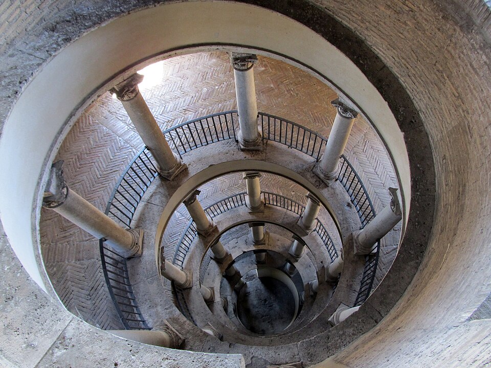 Vista de cima da famosa escadaria em espiral de Bramante na saída dos Museus do Vaticano, com colunas clássicas e piso de tijolos.