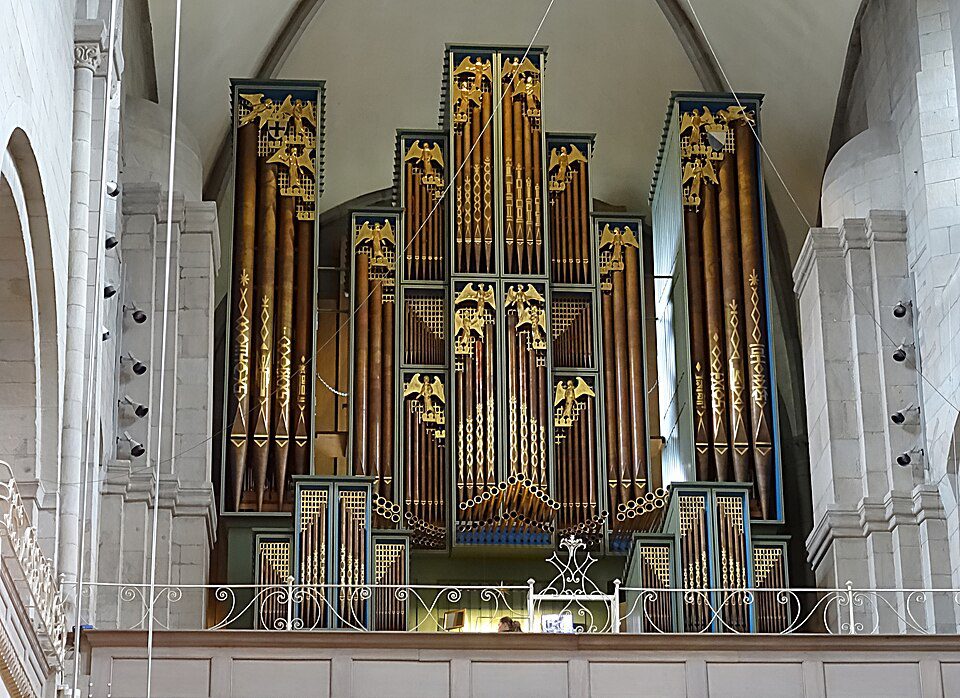 Grande órgão de tubos da Grossmünster em Zurique Suíça, mostrando tubos de bronze verticais, caixilhos decorados com águias douradas e detalhes em verde e azul, localizado na tribuna da catedral
