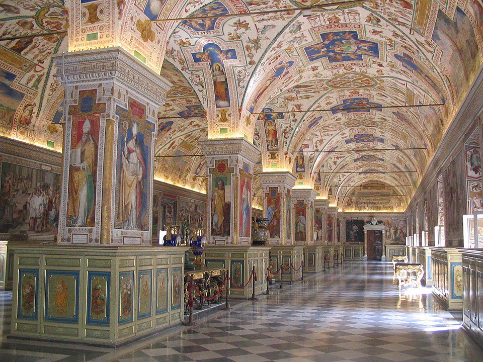 Interior da Sala Sistina da Biblioteca Apostólica Vaticana, com teto abobadado decorado com afrescos, pilares pintados e estantes de madeira.