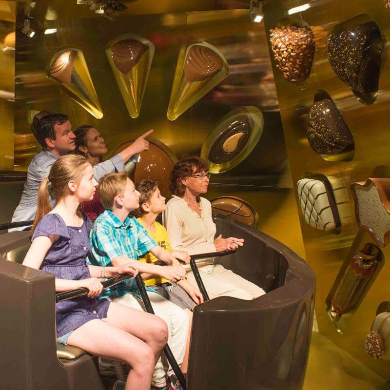 Família em atração turística do Hershey's Chocolate World, sentados em veículo de passeio observando displays iluminados de chocolates e doces