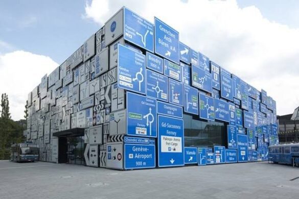 Um edifício cúbico com a fachada inteiramente revestida por placas de sinalização de trânsito azuis e brancas empilhadas.